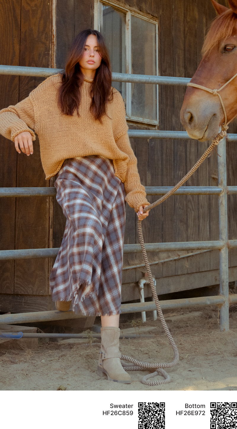 Woman in a cozy sweater and plaid skirt near a horse.