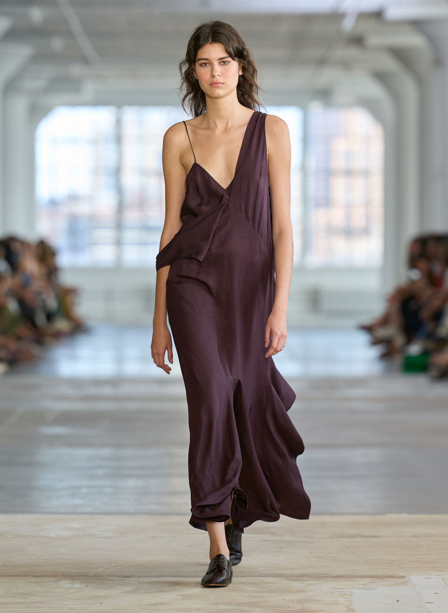 Model walking down runway in a dark purple dress.