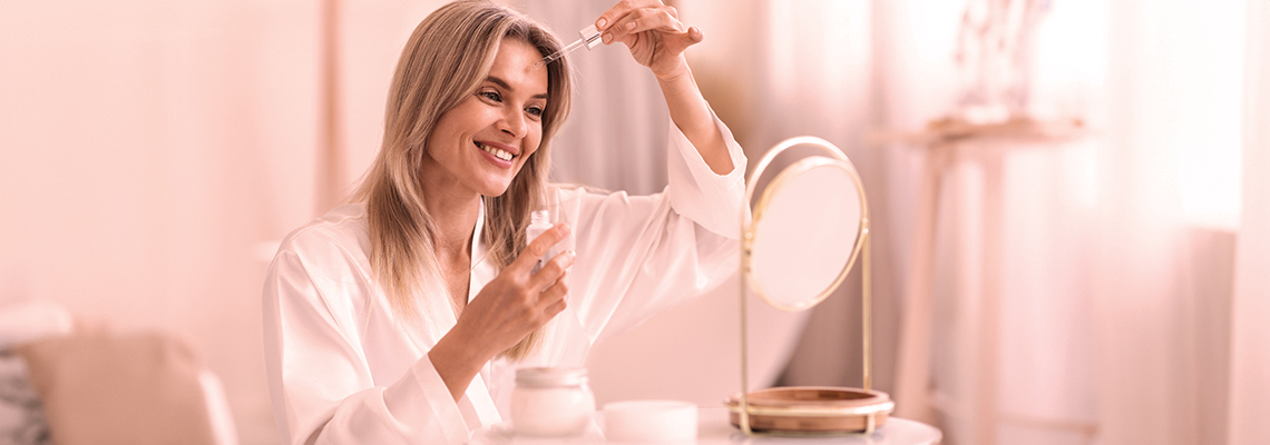 Smiling woman applying makeup in a bright, softly lit room.