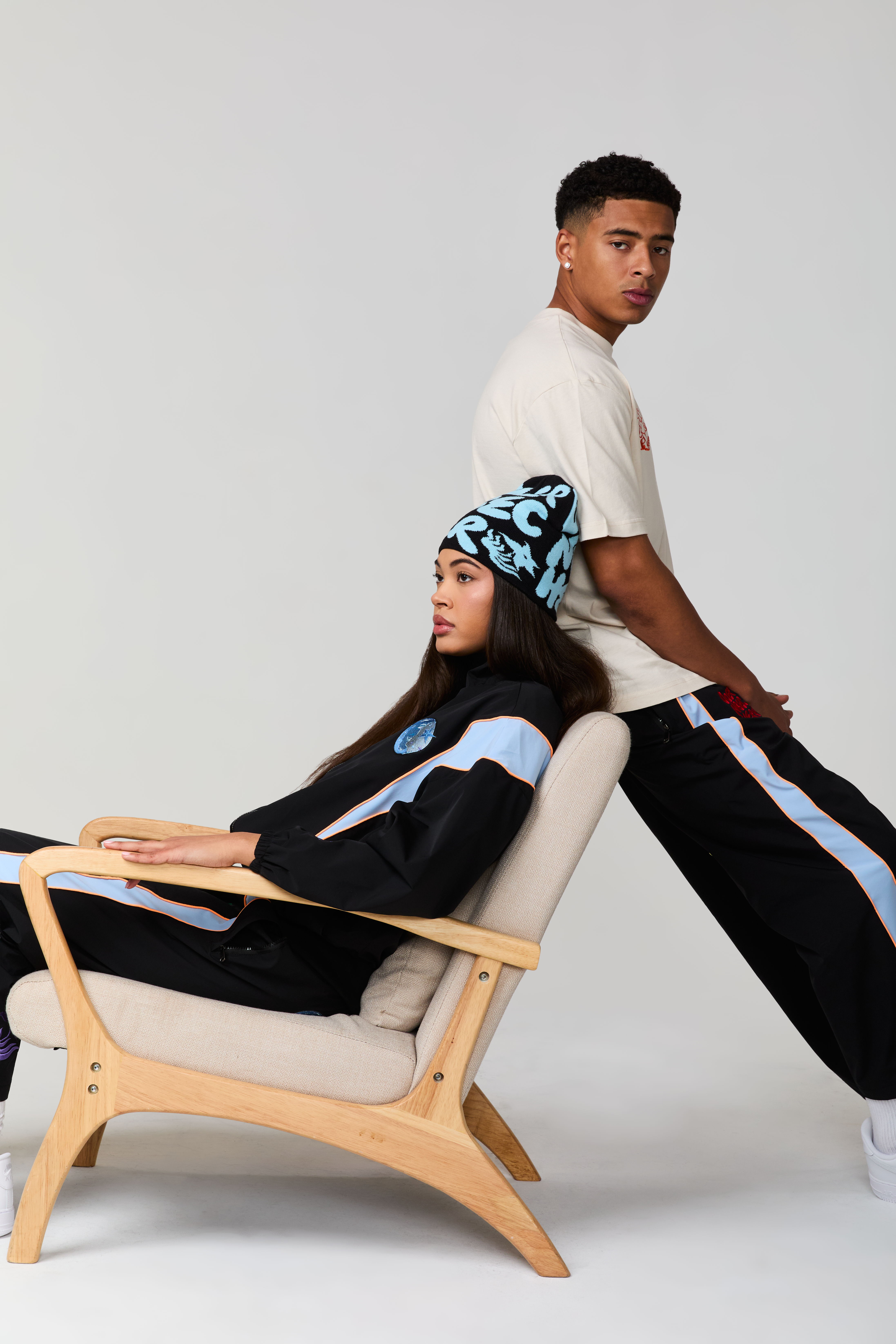 Two young adults posing in casual outfits, seated and standing against a chair.