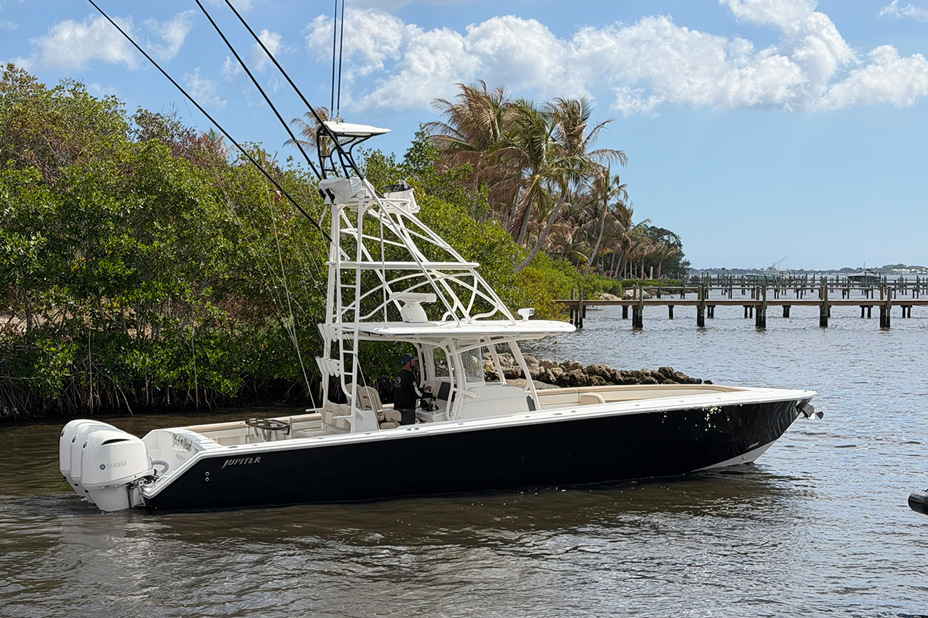 Black and white Jupiter center console fishing boat with dual Yamaha outboards and a custom tuna tower floating in calm South Florida backwater near mangroves and docks under a bright blue sky with scattered clouds.