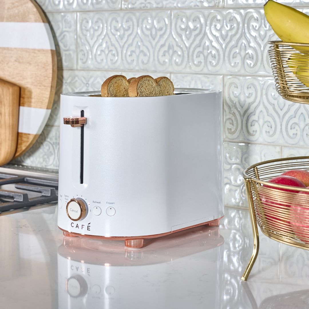 Matte white toaster with toast and a bowl of fruit nearby.