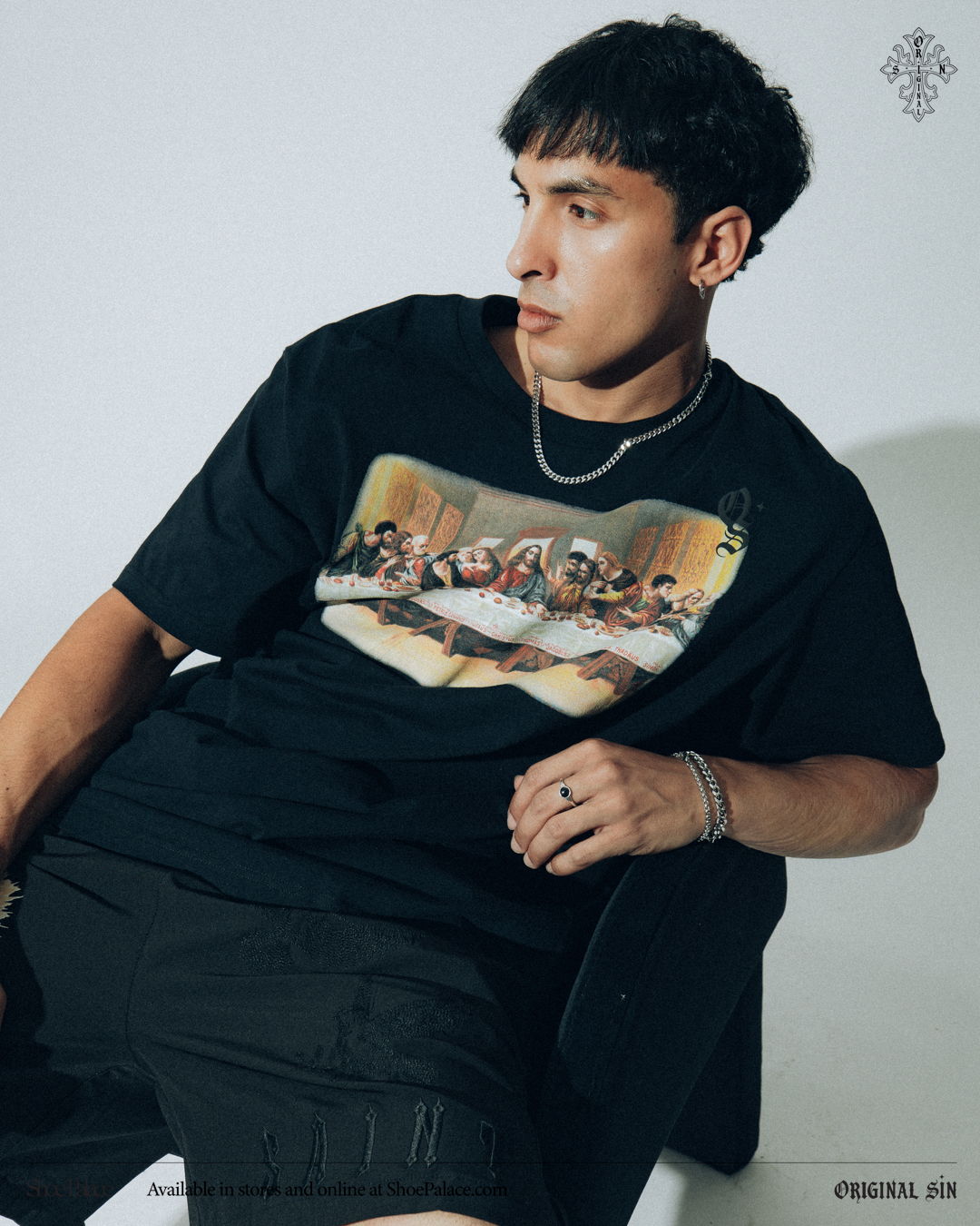 Young man in a black graphic t-shirt, sitting against a white background.