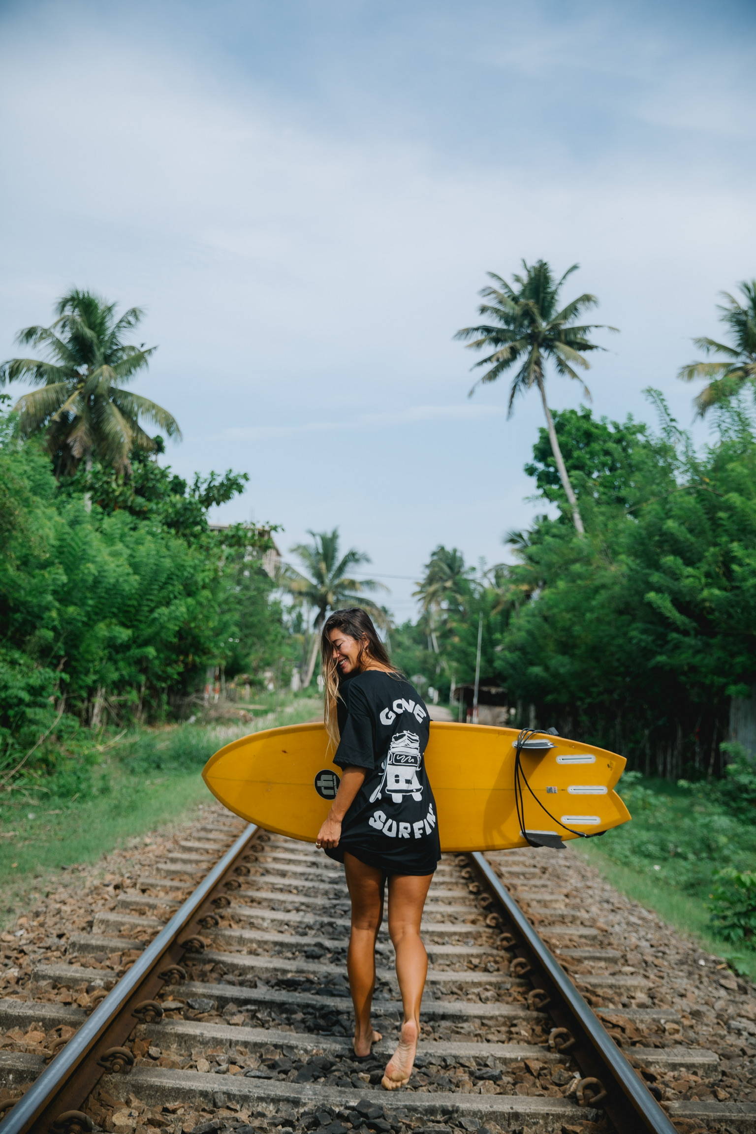 A woman holding her yellow surfboard on train tracks in Sri Lanka