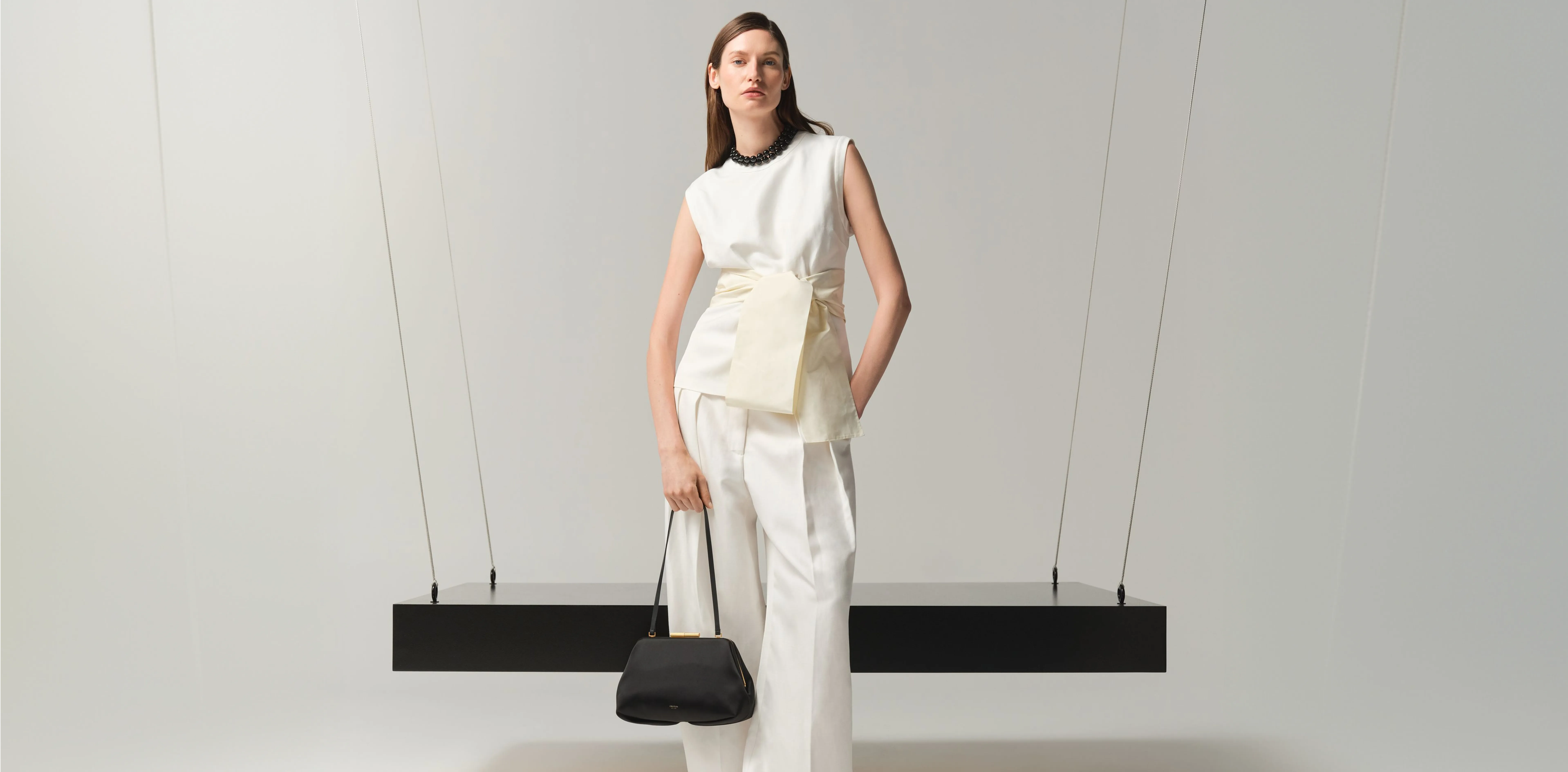 Model wearing stylish outfit with a handbag, standing against a minimalist background.