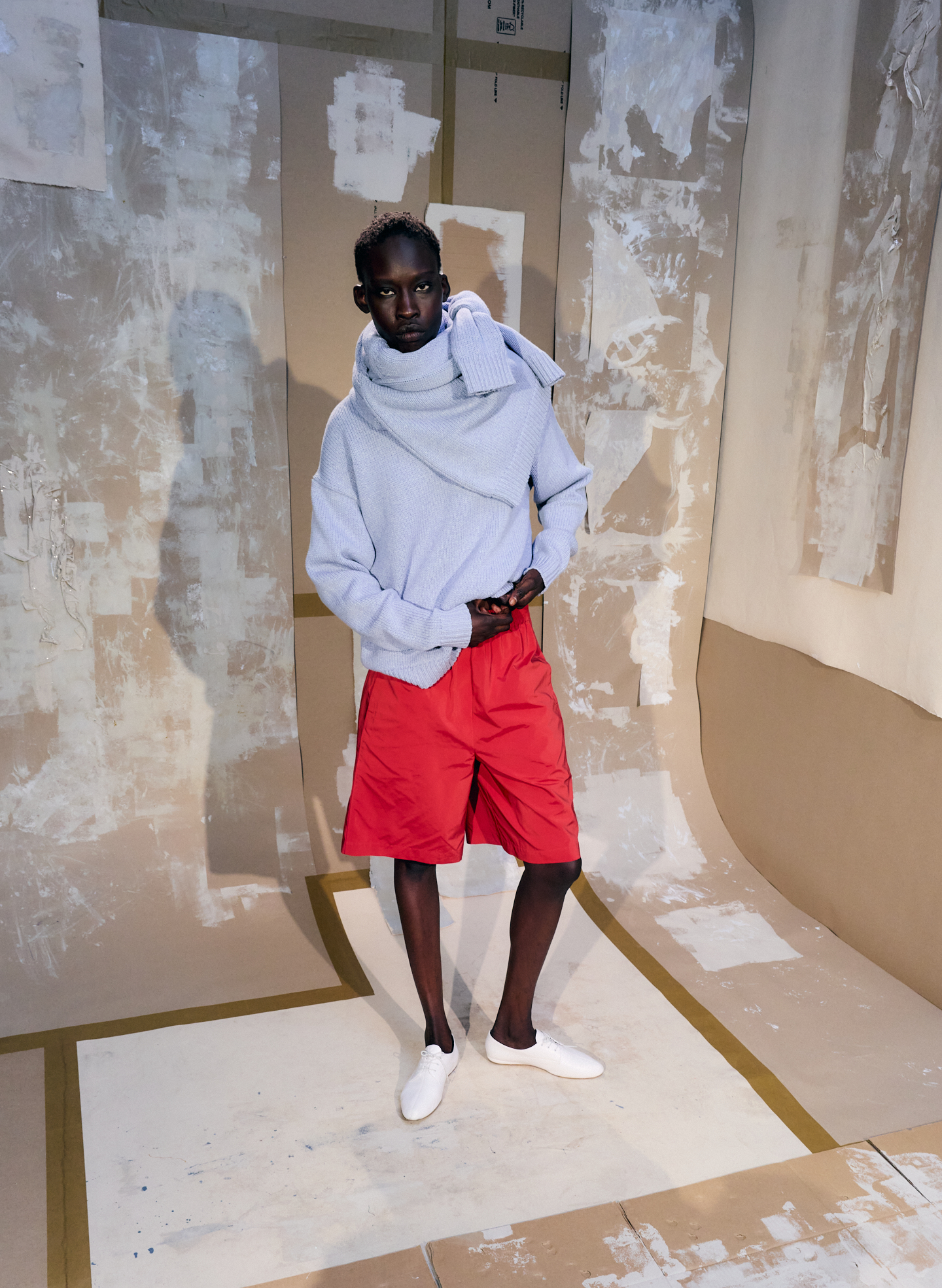Model wearing a gray hoodie and red shorts in a textured background.
