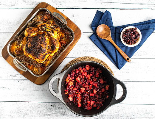 Roasted chicken with cranberry sauce and side ingredients on a white table.