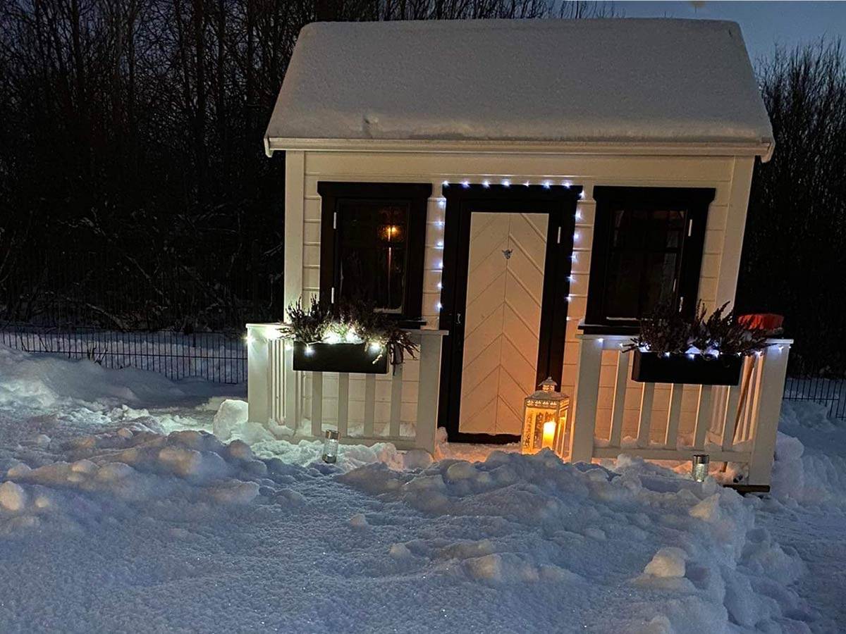 White and black custom wooden playhouse with black flower boxes and lights in the  snowy backyard by WholeWoodPlayhouses