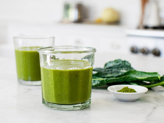 Two glasses of Matcha smoothie on a marble countertop with leafy greens.