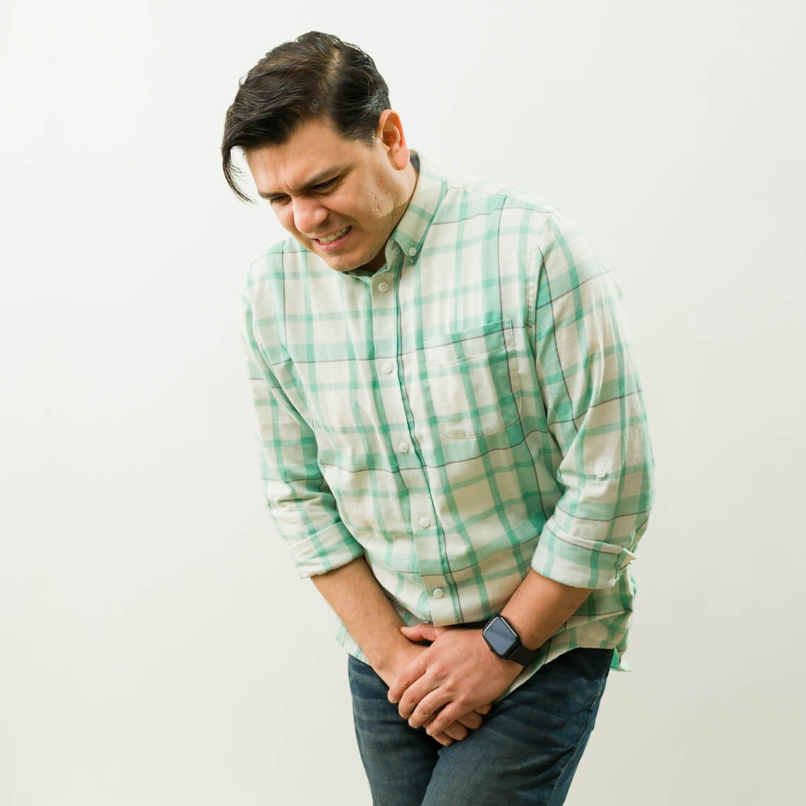 Man in a green checked shirt appears to be in discomfort.