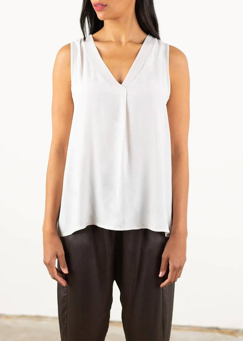 A model wearing an oatmeal coloured v neck sleeveless top with dark grey satin trousers