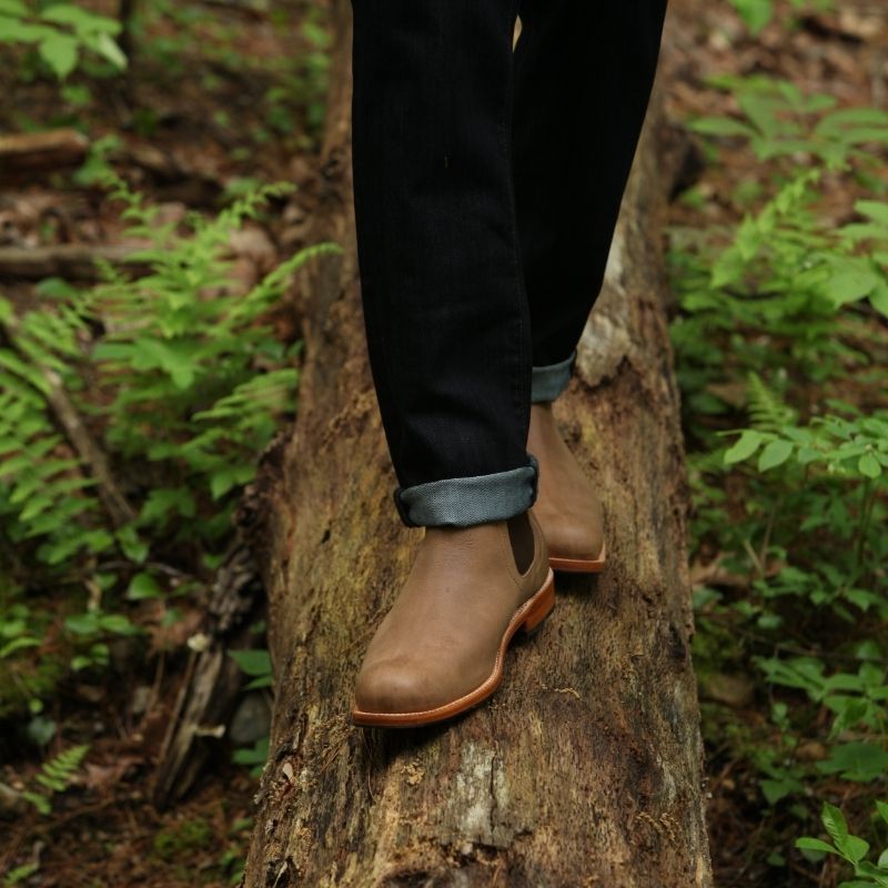 A man balancing on a fallen log in the woods wearing Adelante light brown leather wide width Chelsea boots.
