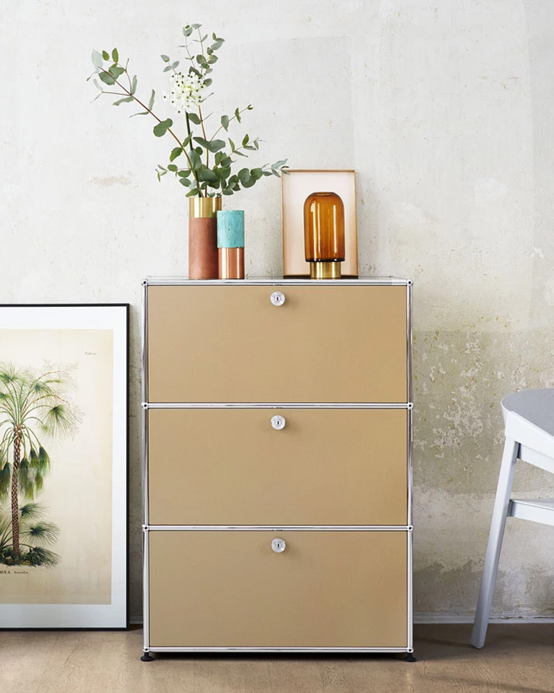 Three-drawer USM filing cabinet in dark color with circular handles.