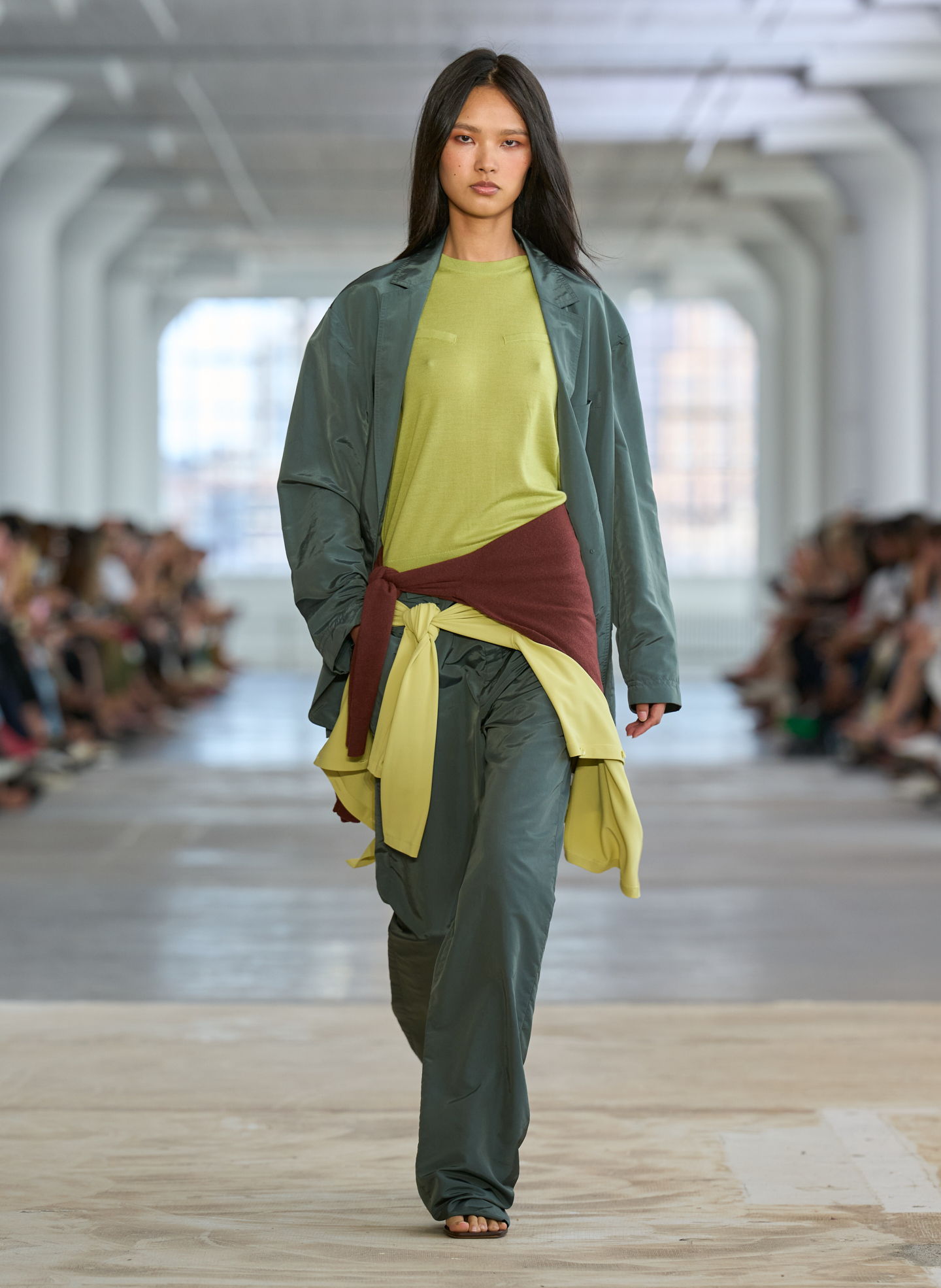 A model walking on a runway, wearing layered clothing in green and yellow.
