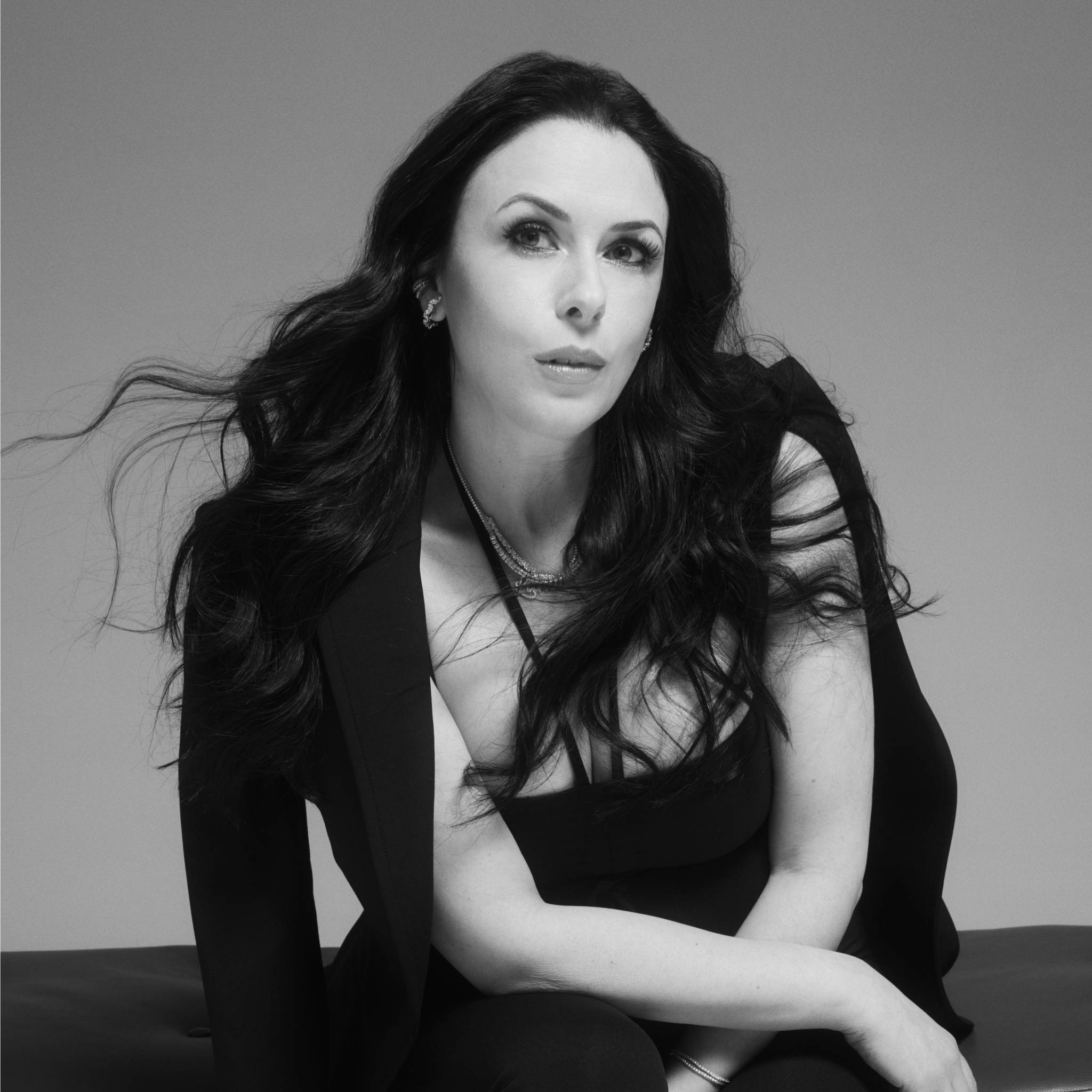 Lana in black attire, sitting against a gray background.