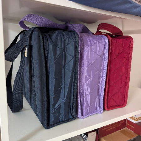 3 colors of carry-all binder bags on a shelf, bue, purple and red