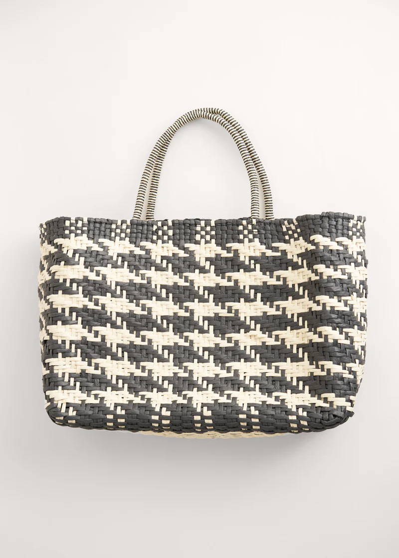 A wicker shopper basket with a black and off white houndstooth pattern and striped handles