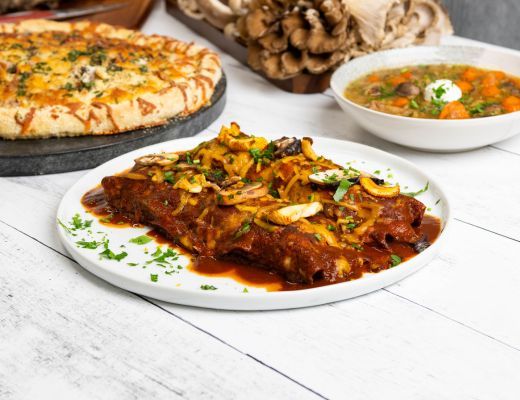A plate of enchiladas with sides of pizza and soup.