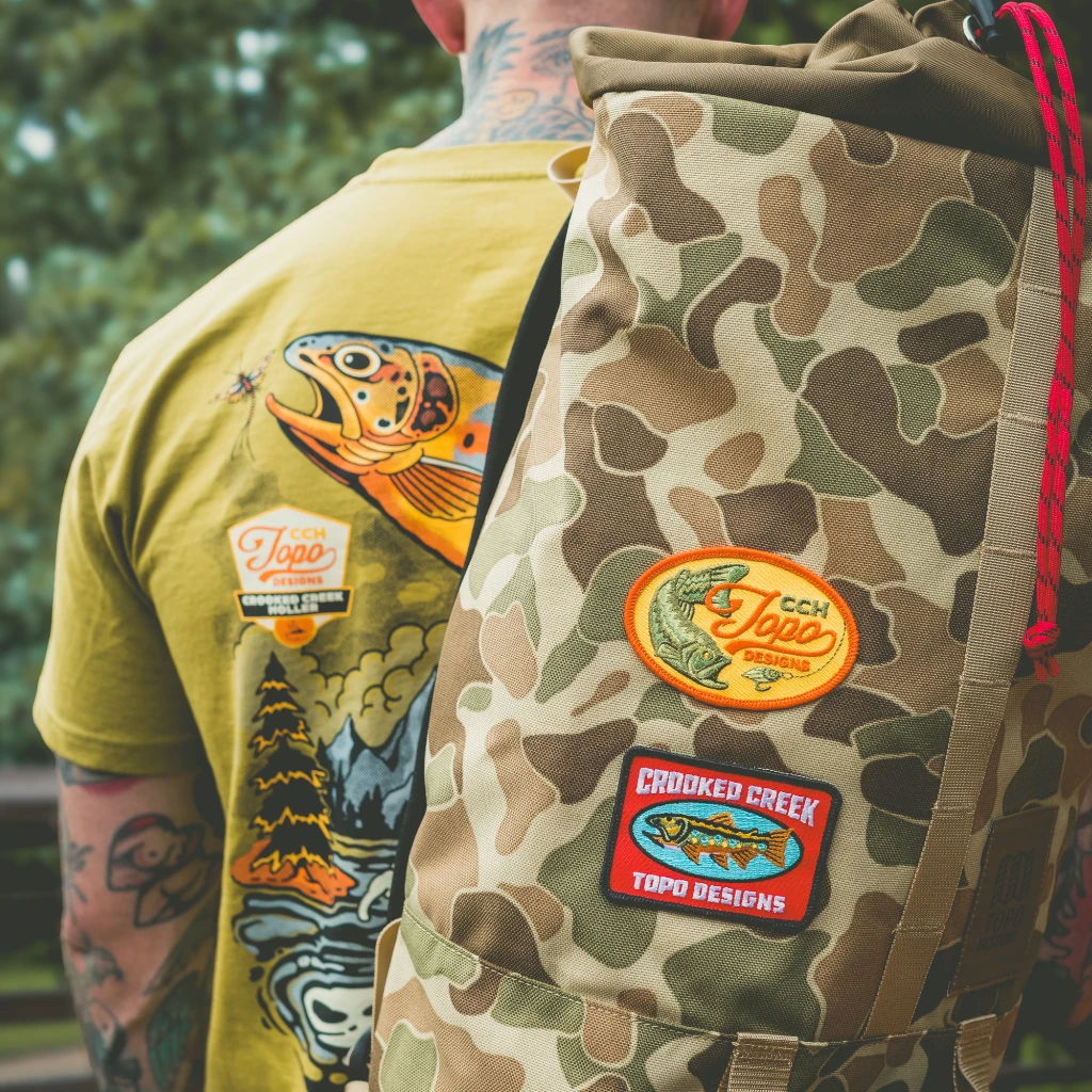 Person wearing a yellow shirt with fish graphics and a camo backpack.