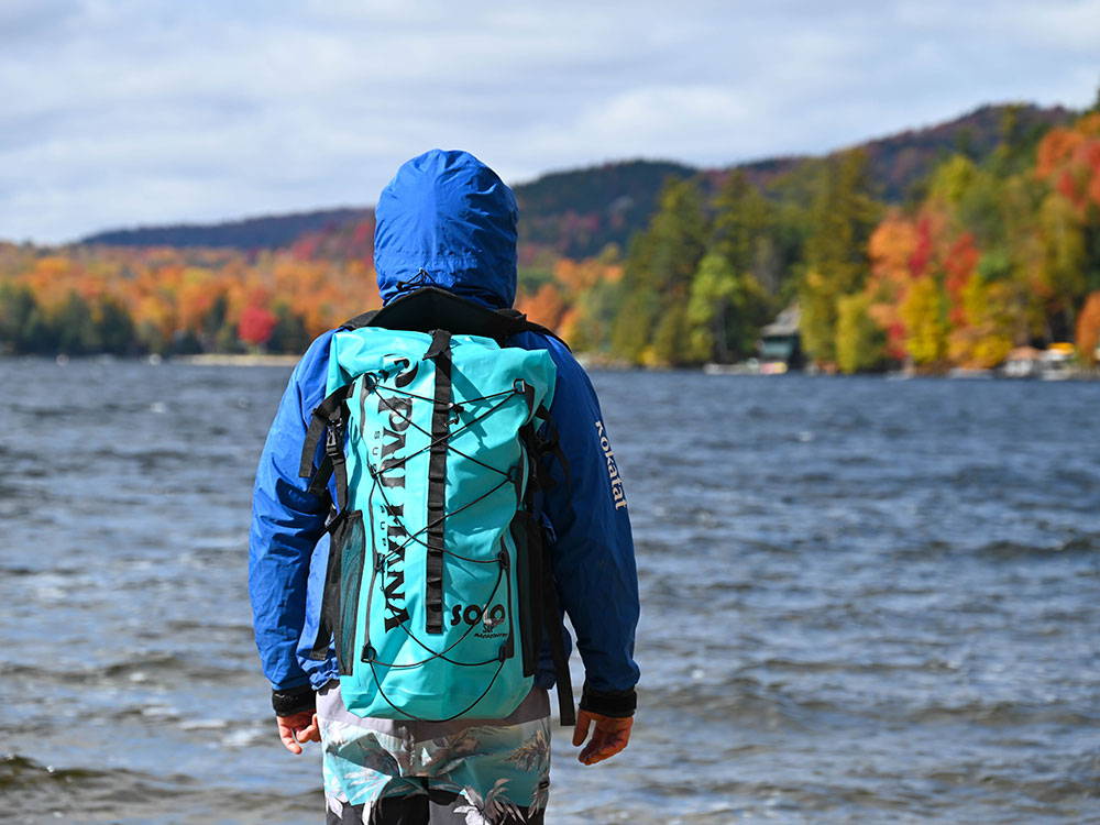 Man standing in front of lake with a pau hana backpack on with autumn colors in the background