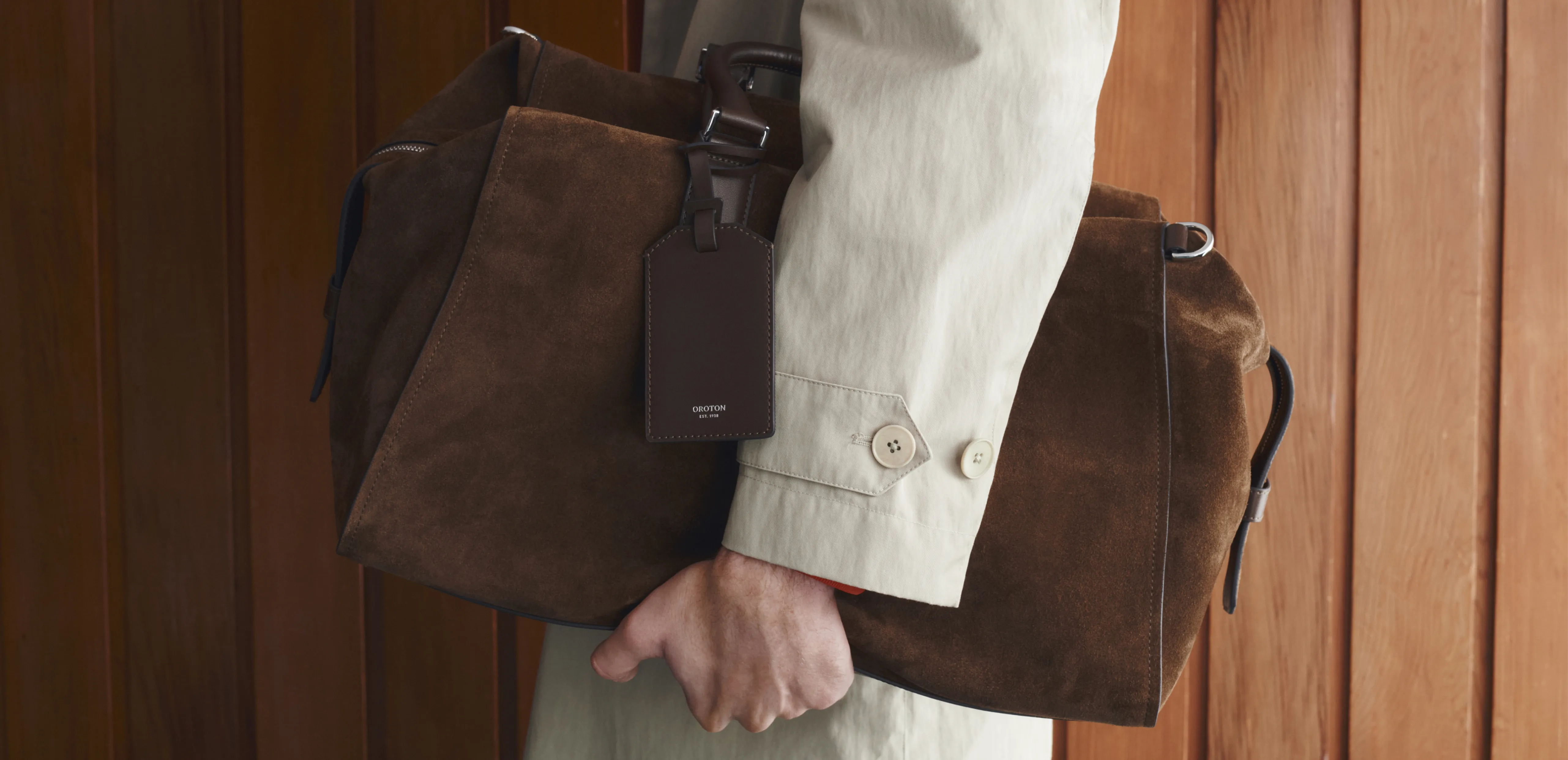 Person holding a brown suede bag against a wooden background.