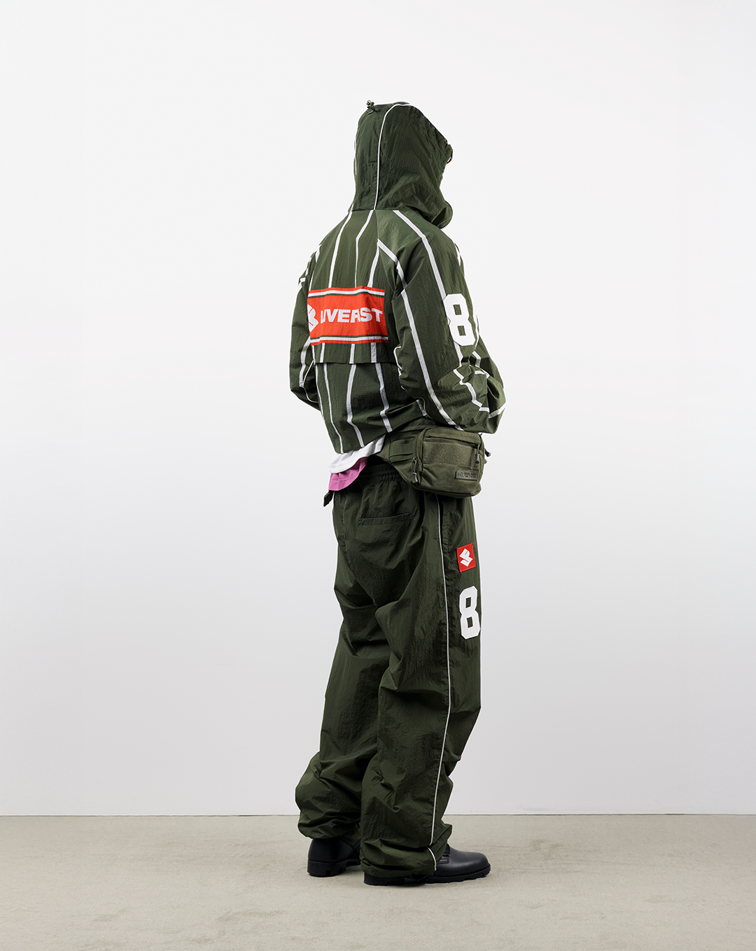 A person wearing a green outfit with a hood, standing against a white background.