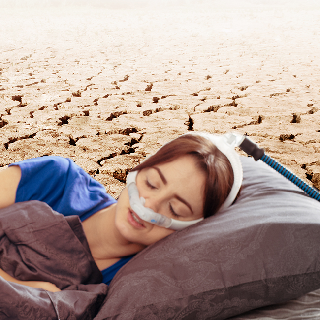 Woman sleeping with a CPAP mask against a cracked-earth backdrop illustrating CPAP dry mouth