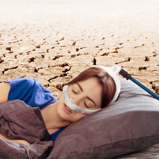 Person sleeping on a bed in a dry, cracked landscape.