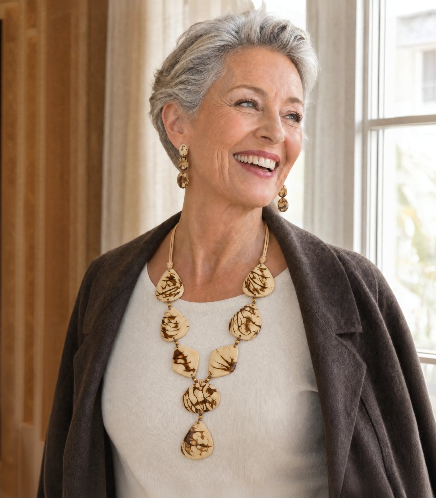Smiling woman in a cream sweater and brown jacket wearing a tagua statement necklace and matching earrings