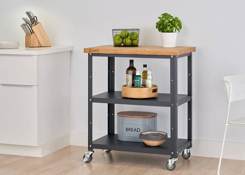 Kitchen cart with items on its shelves and bamboo cutting board on top