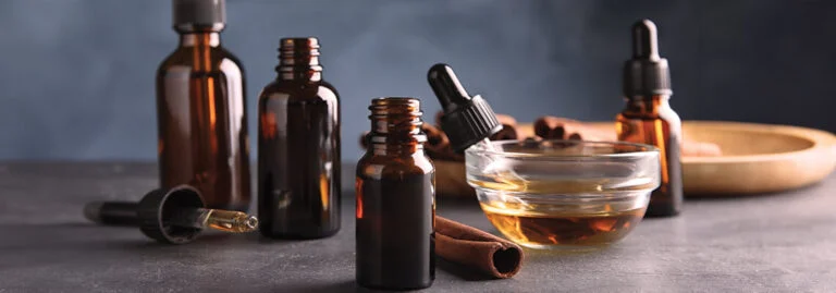 Brown glass bottles and a bowl of oil on a dark surface.