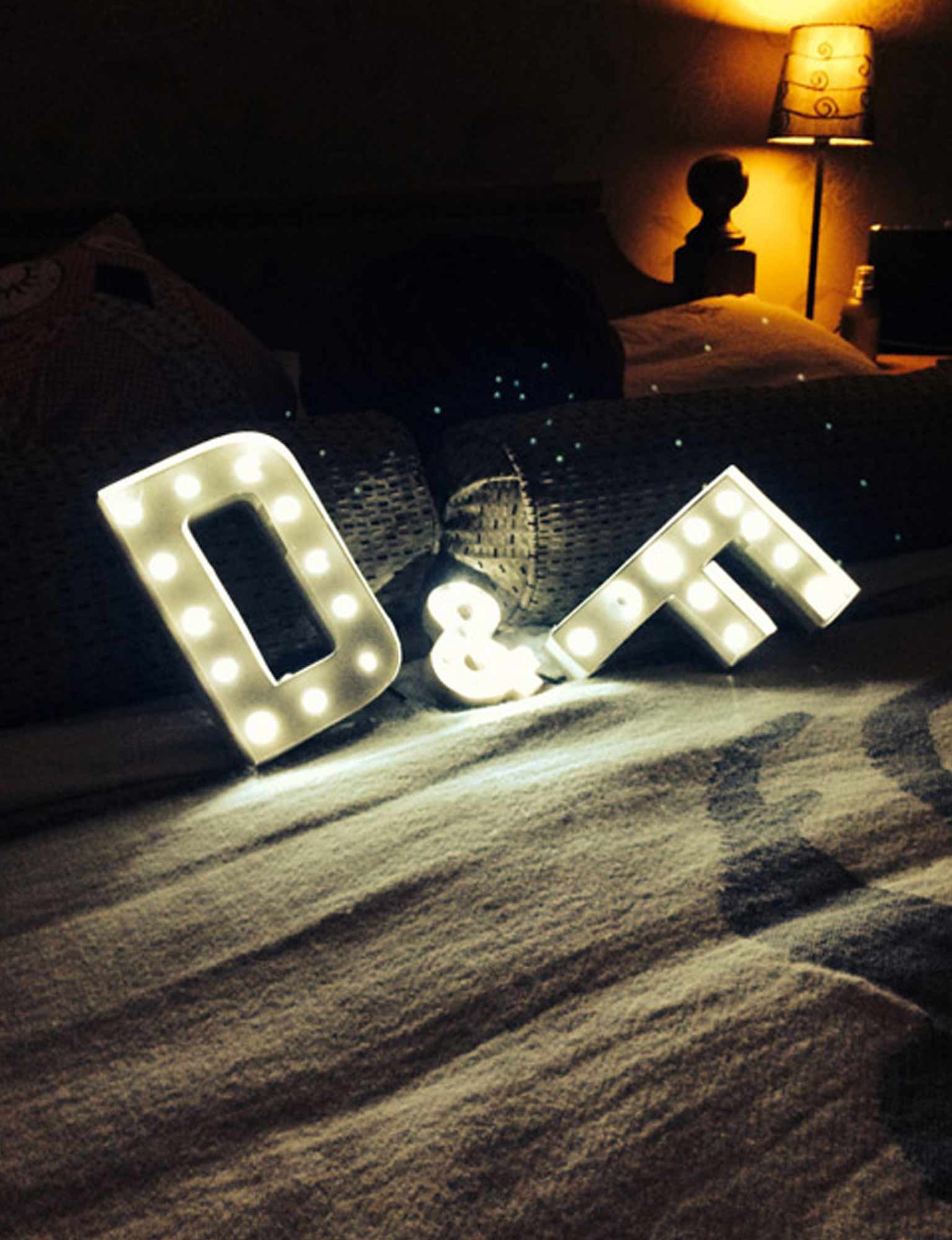 D and F light up letters on a bed with fairy lights in the backdrop.
