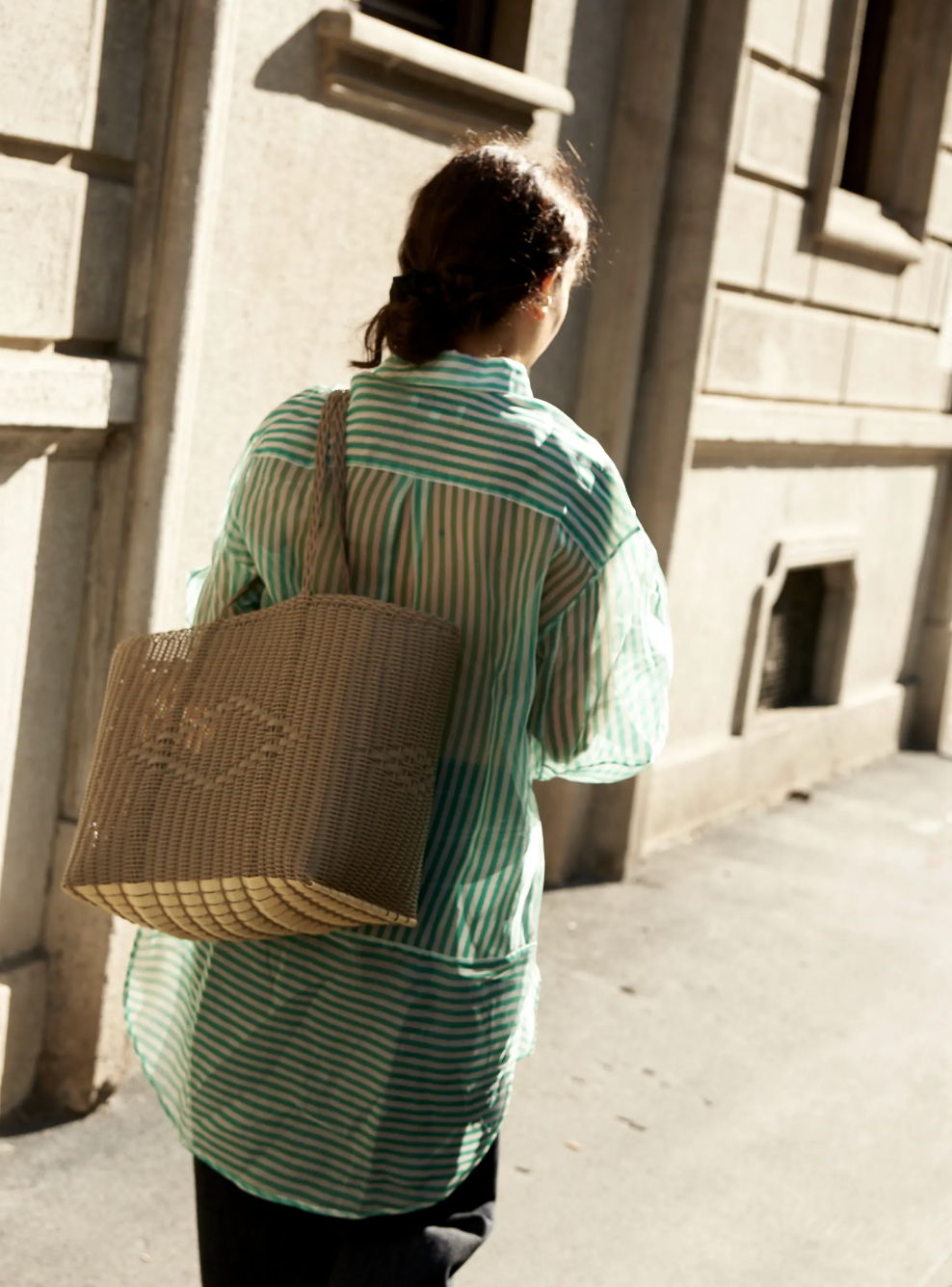 A woman walks away, wearing a striped shirt and carrying a tote bag.