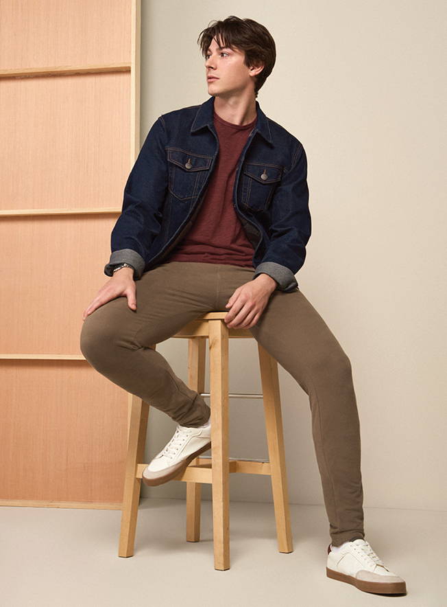 Tall man sitting on a stool wearing a denim jacket and sweatpants 