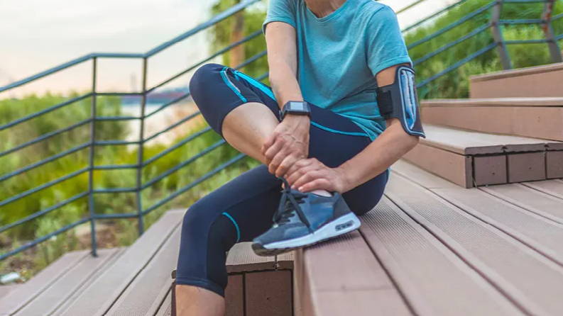 Woman grabbing shin in pain while sitting on steps