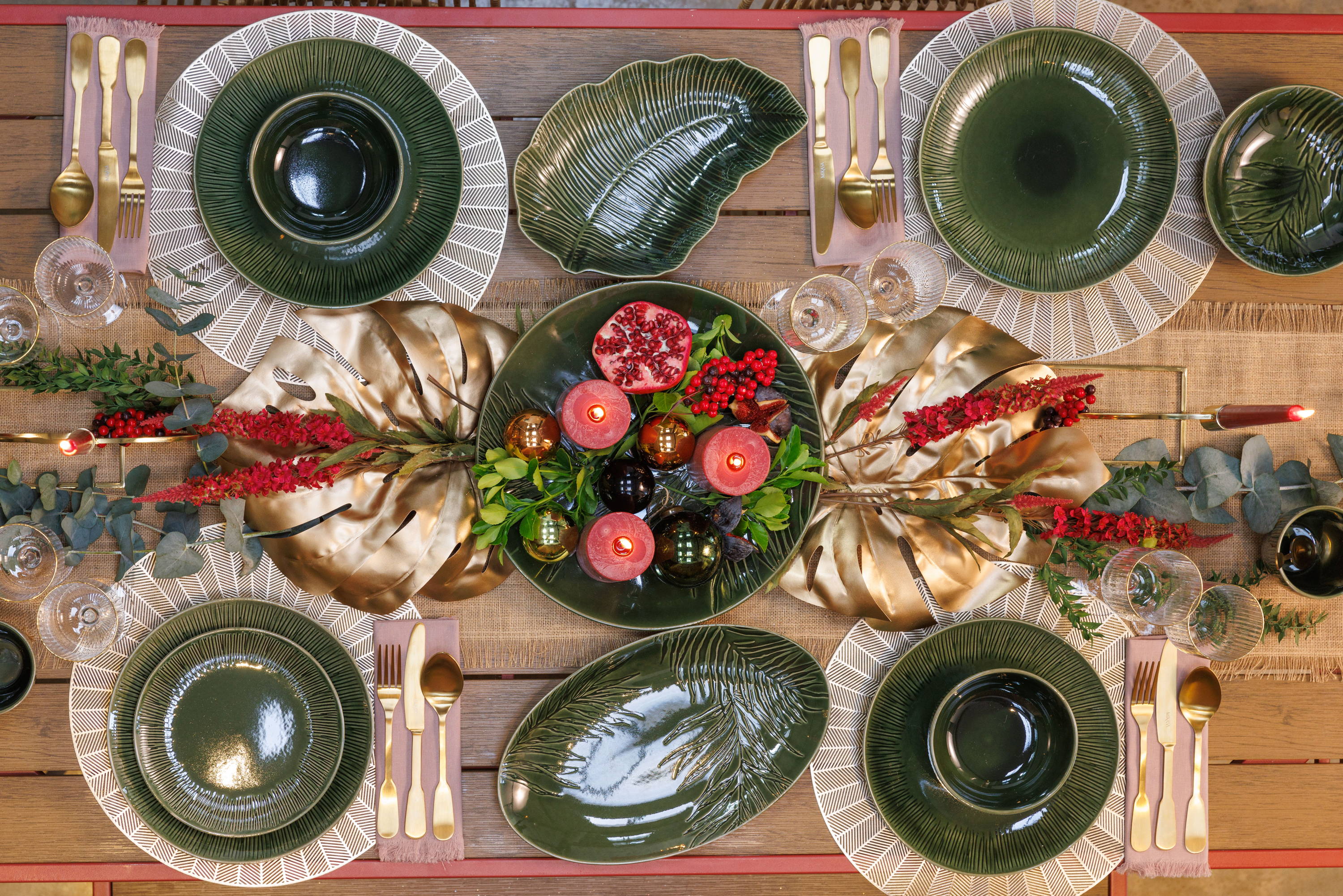 A dining table with green plates, gold plates, gold cutlery and candles and foliage as the centrepiece.