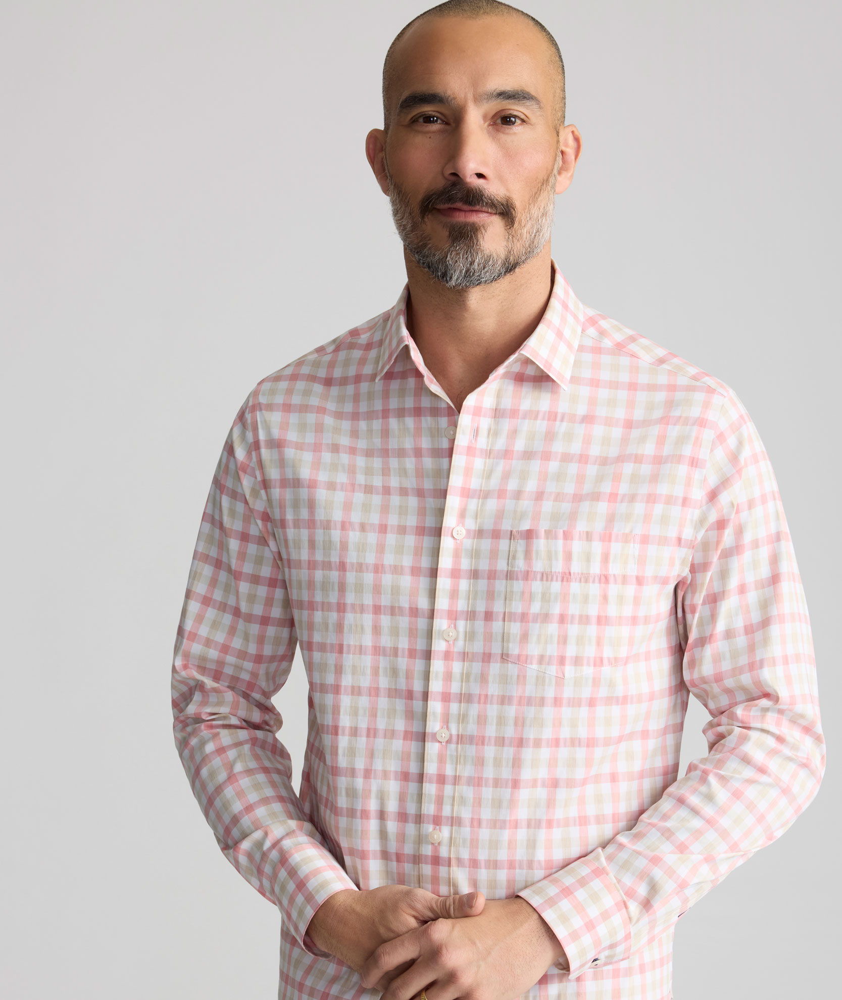 A man in a checked shirt standing with hands clasped.