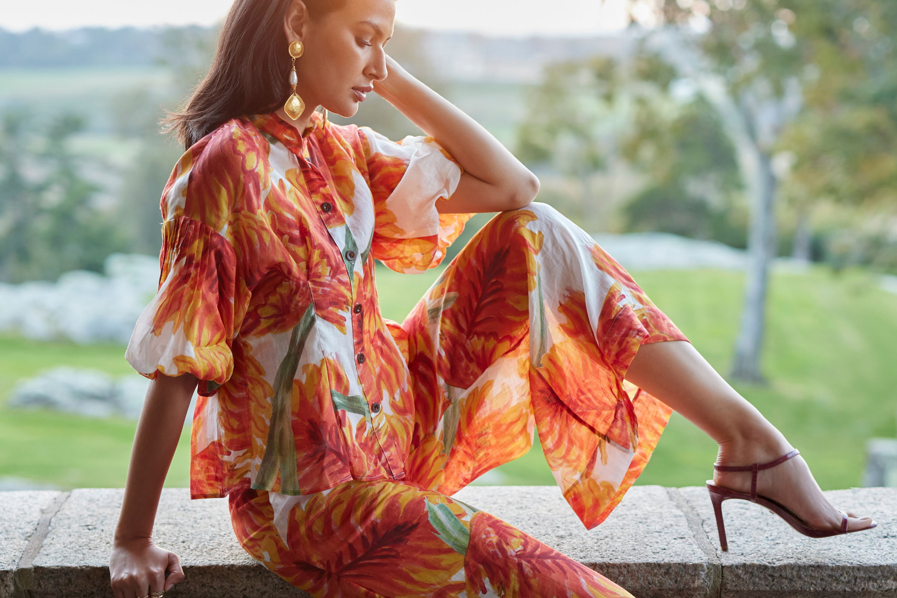 Woman in colorful floral outfit sitting outdoors with nature in the background.
