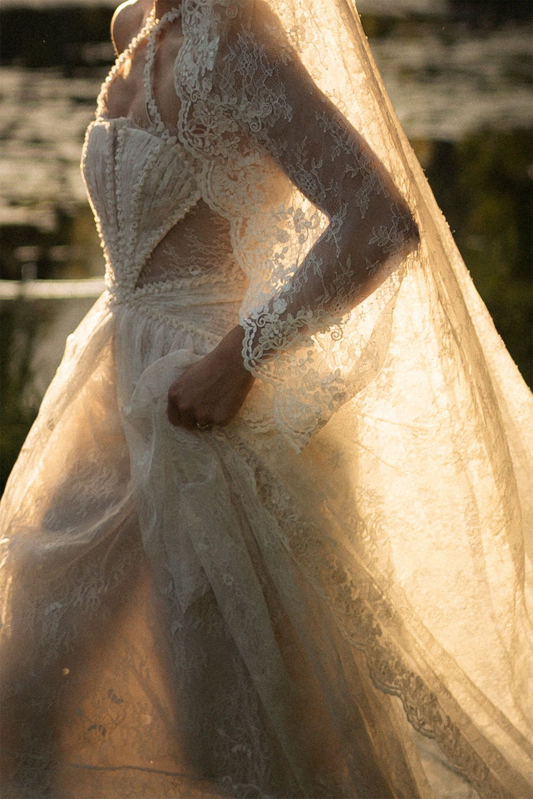 A woman in a flowing lace wedding dress illuminated by soft sunlight.