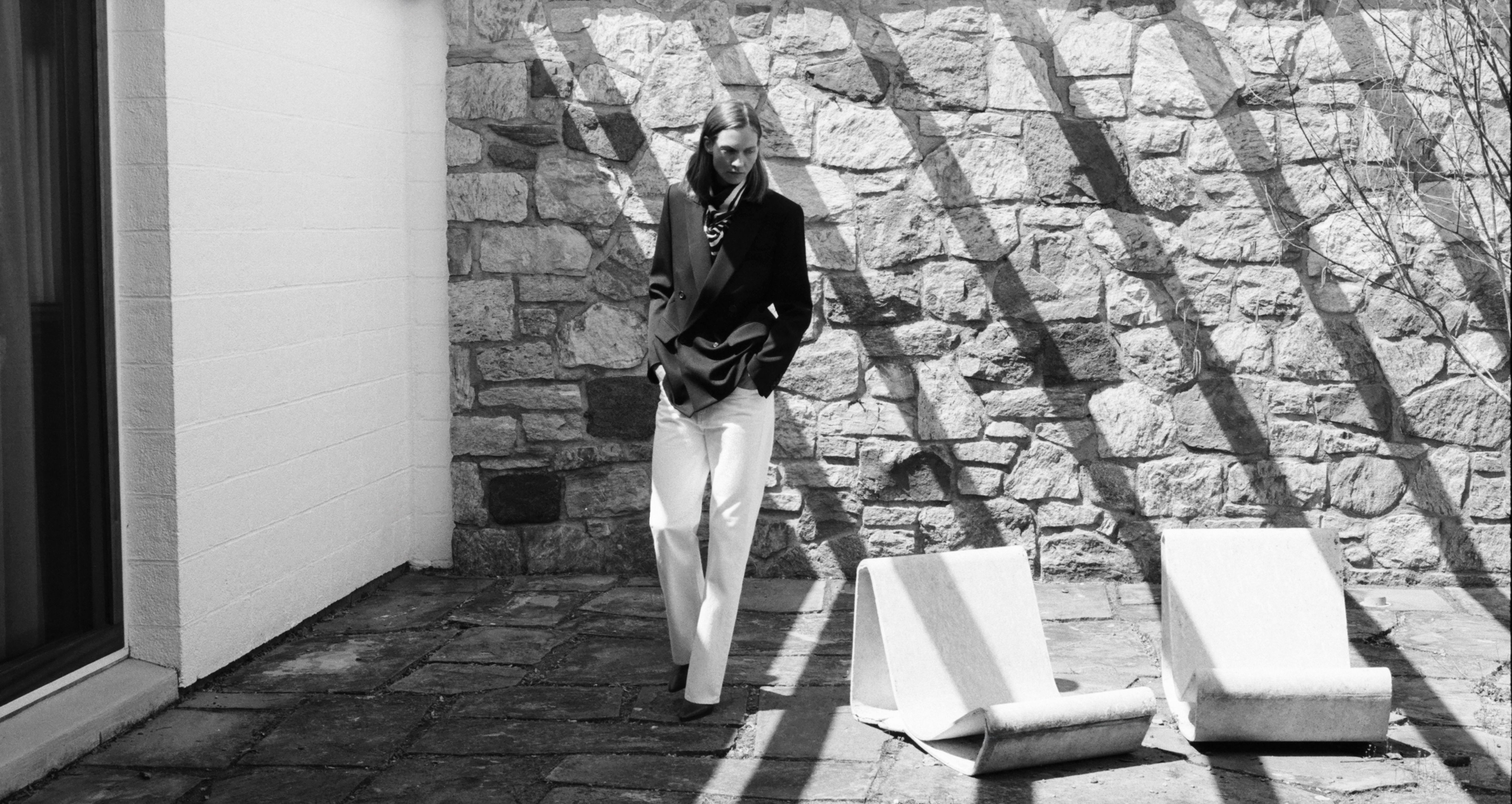 Person in black outfit standing near stone wall with shadows.