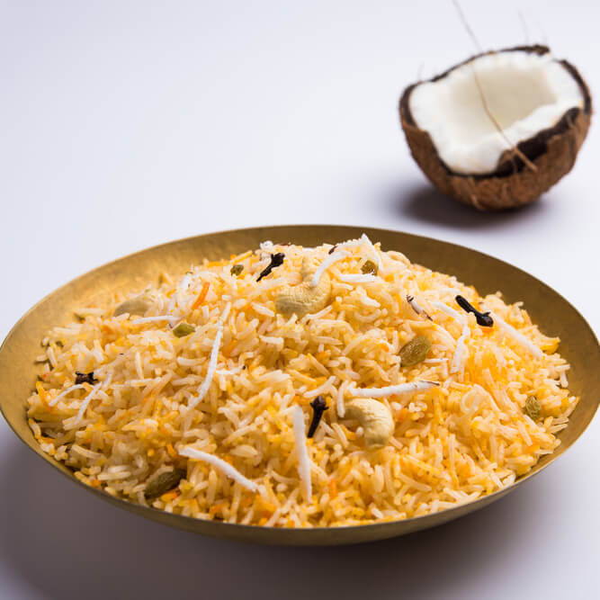 a bowl of golden rice with cardamom and a coconut half in the background