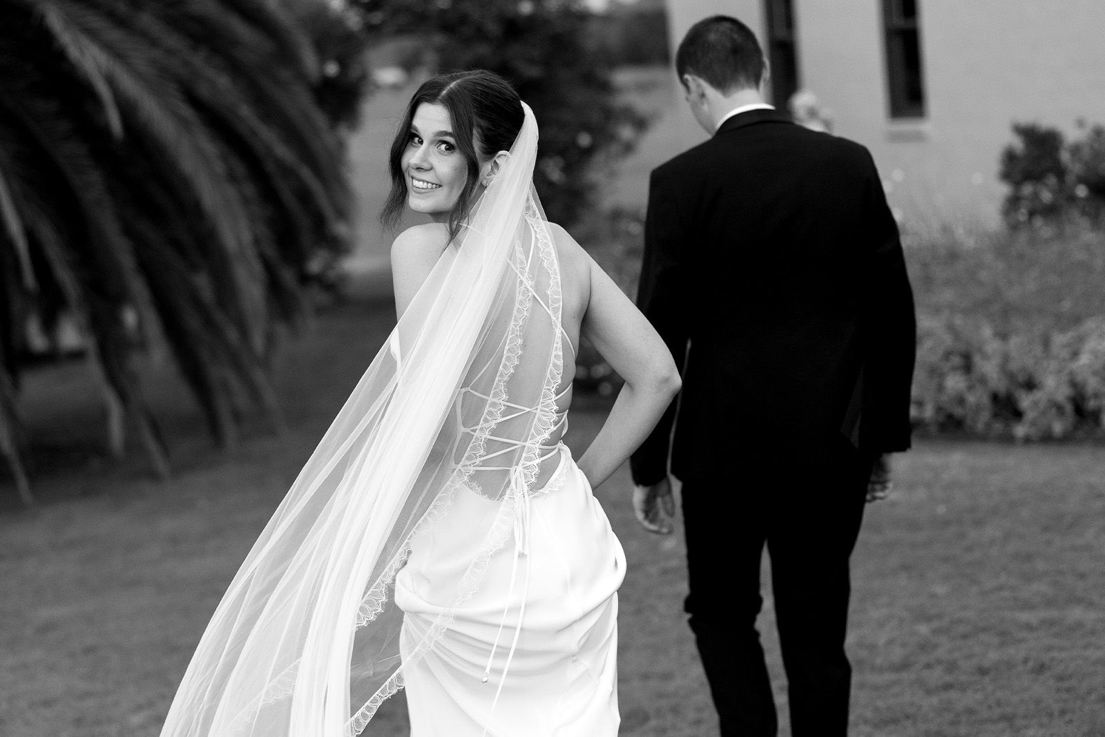 Bride looking back at groom, wearing a veil and wedding dress.