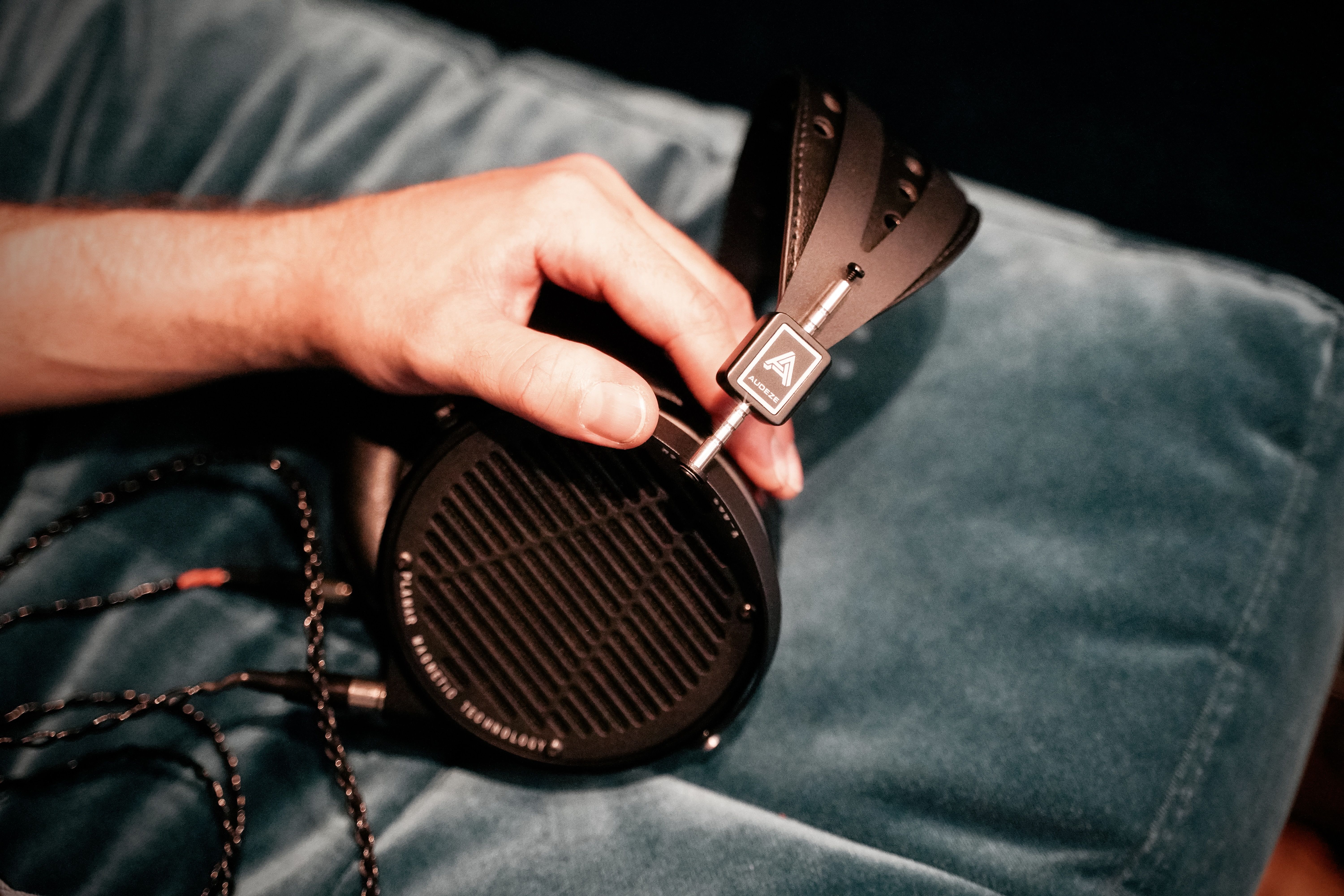 A hand holding a Audeze LCD-X headphone on a soft surface