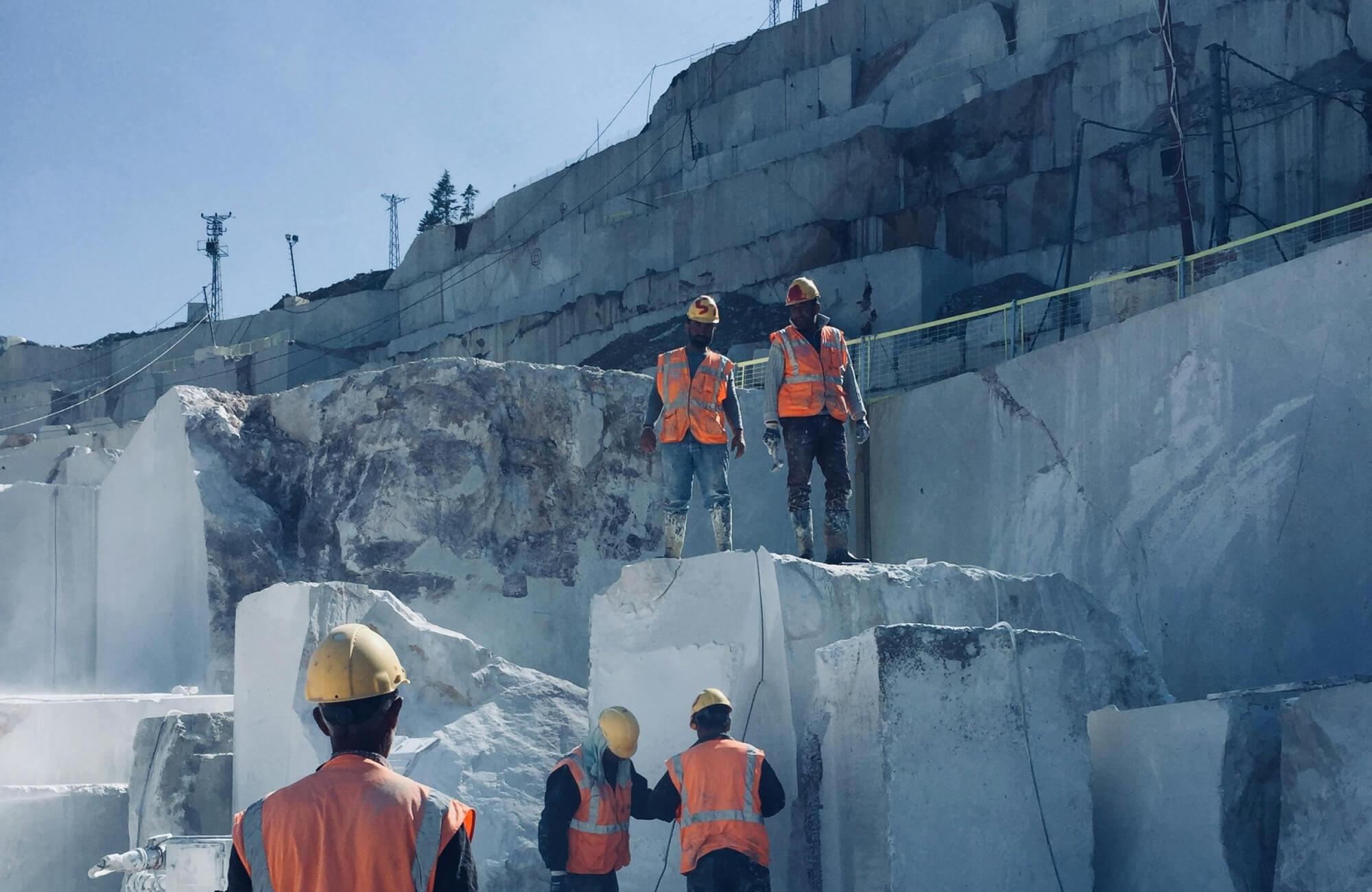 Mining workers wearing hard hats and high-visibility safety gear inside an active quarry