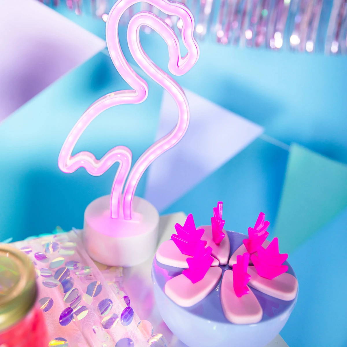 Luz de néon de flamingo ao lado de uma taça de agitadores de bebidas em forma de flamingo, adicionando um brilho cor-de-rosa vibrante ao ambiente.