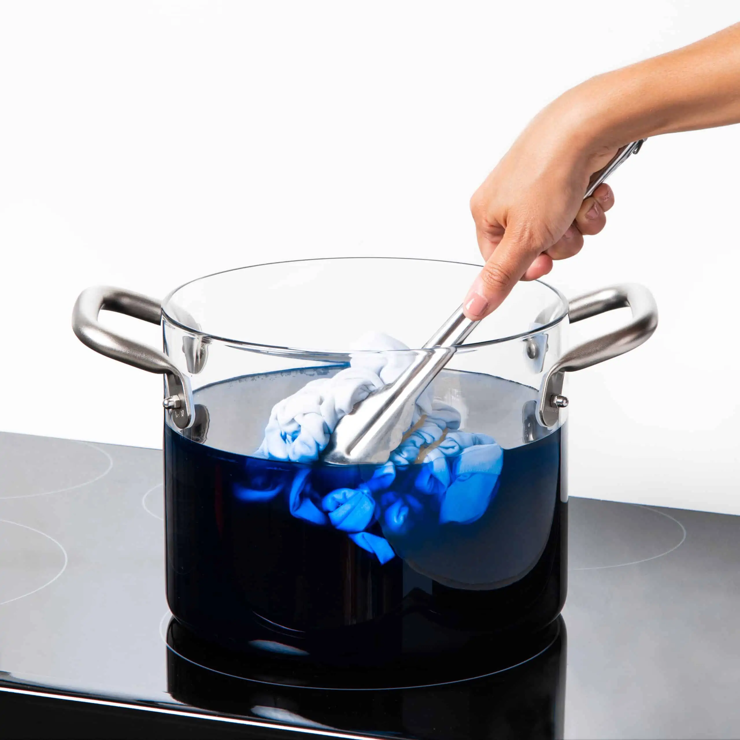 Hand stirring blue fabric in a pot of dark dye.