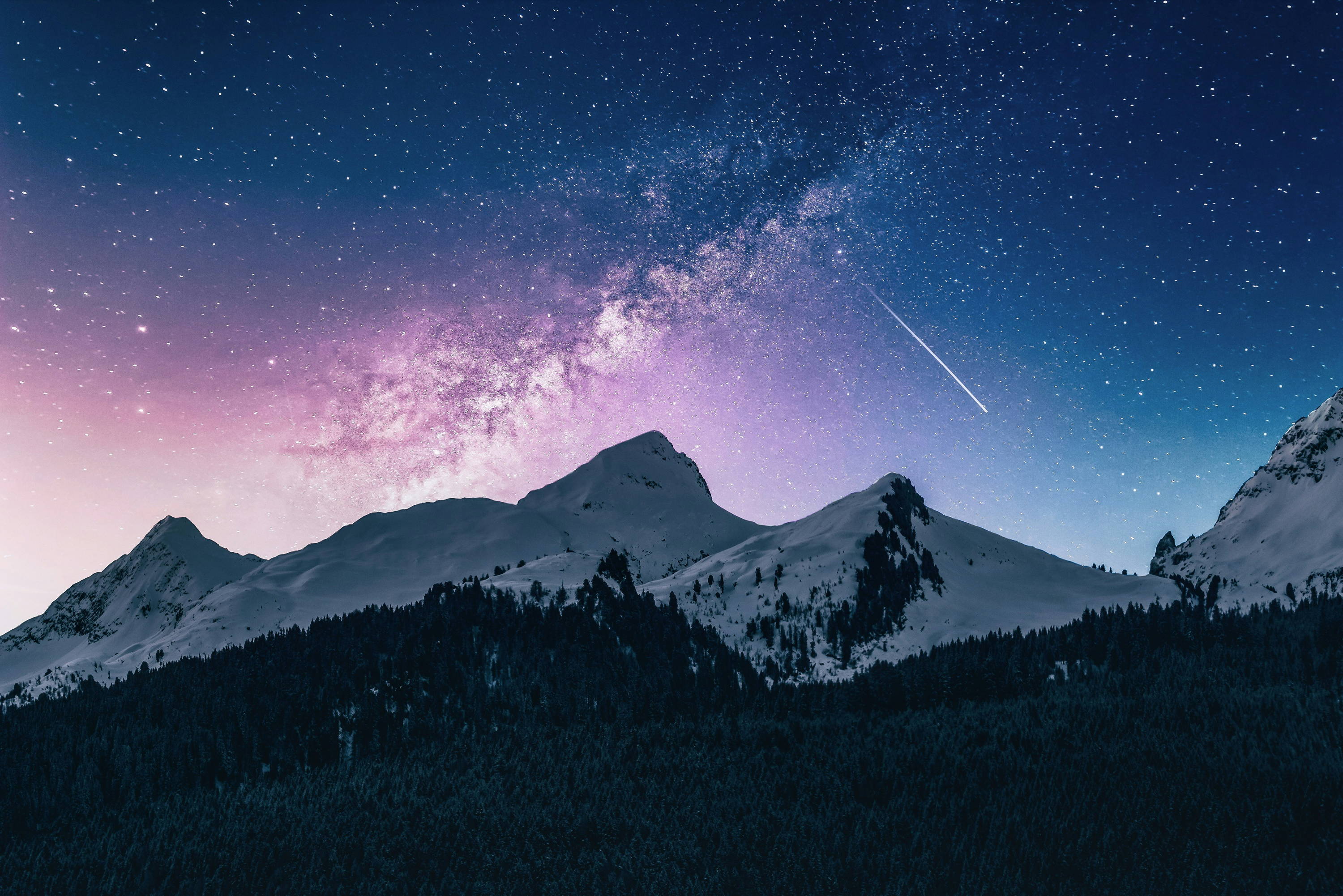A bright, starry sky behind a snowy mountain range. 