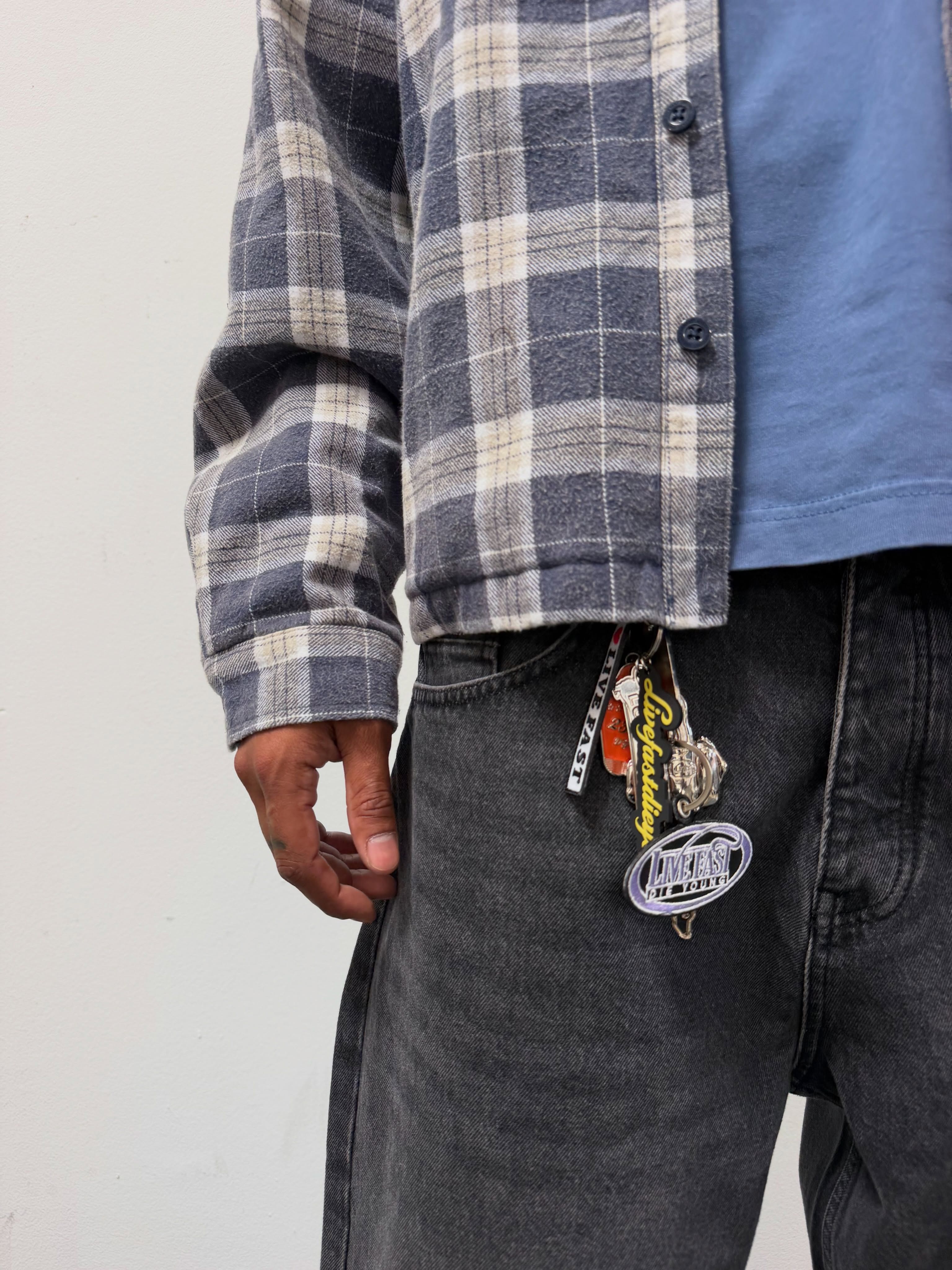 Person wearing a plaid shirt and gray pants with decorative keychain.