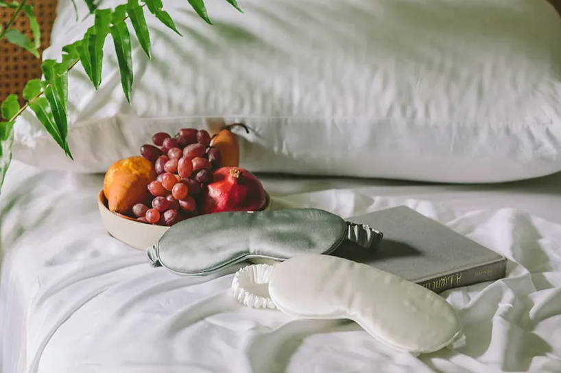 the silk luxury sleep masks resting on white bedding and a grey book