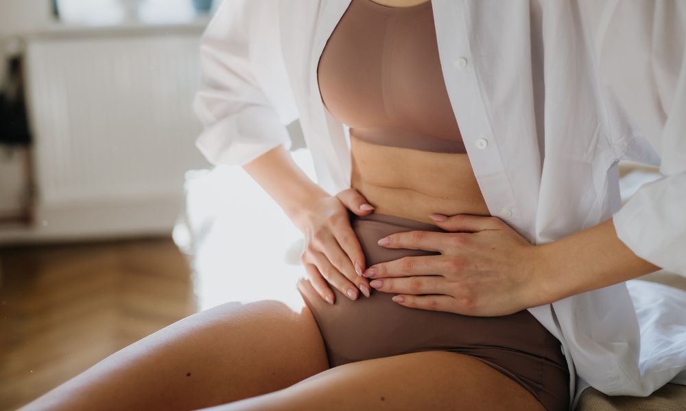 Person in a brown outfit holding their stomach, showing discomfort.